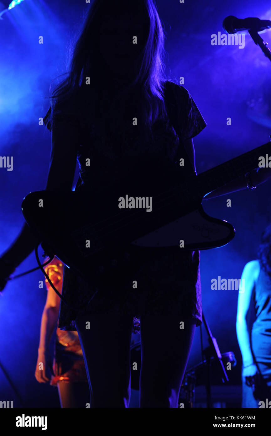A female guitarist in a band silhouetted by blue stage lights Stock