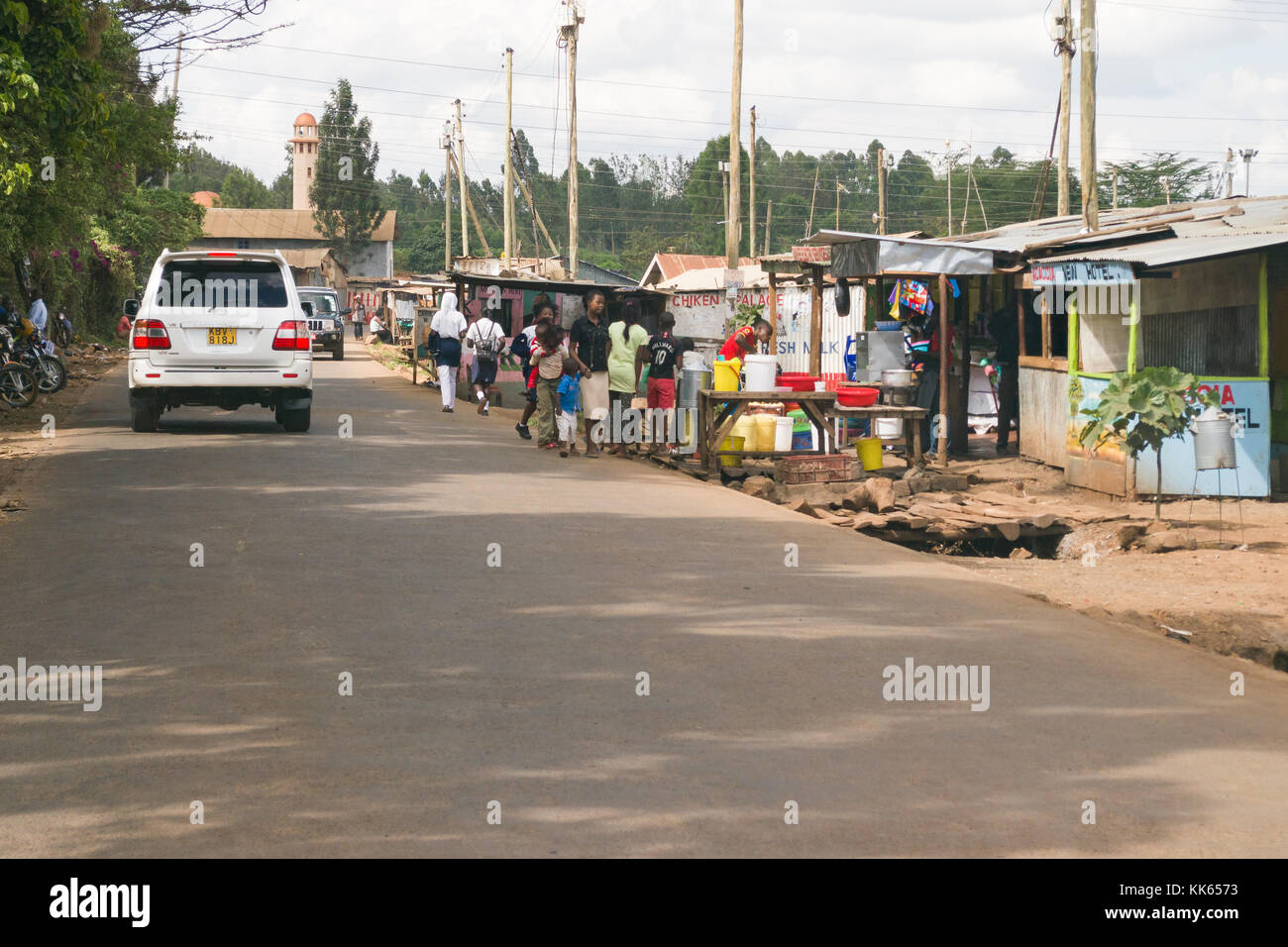 Vehicles drive along a road alongside Githogoro village slum with people going about daily life, Kenya, East Africa Stock Photo