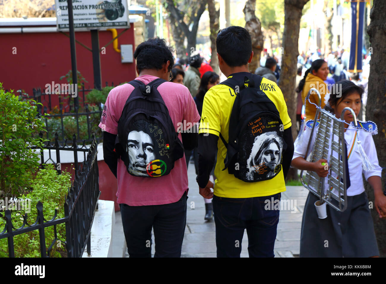 Youths wearing rucksacks with faces of Jimi Hendrix (L) and Kurt Cobain (R) on them walking in street, La Paz, Bolivia Stock Photo