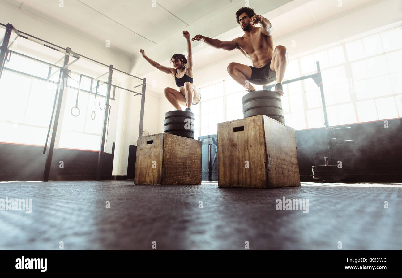 Young athletes box jumping at cross training gym. fitness man and woman doing a box squat at the gym. fitness couple doing intense exercise at health Stock Photo