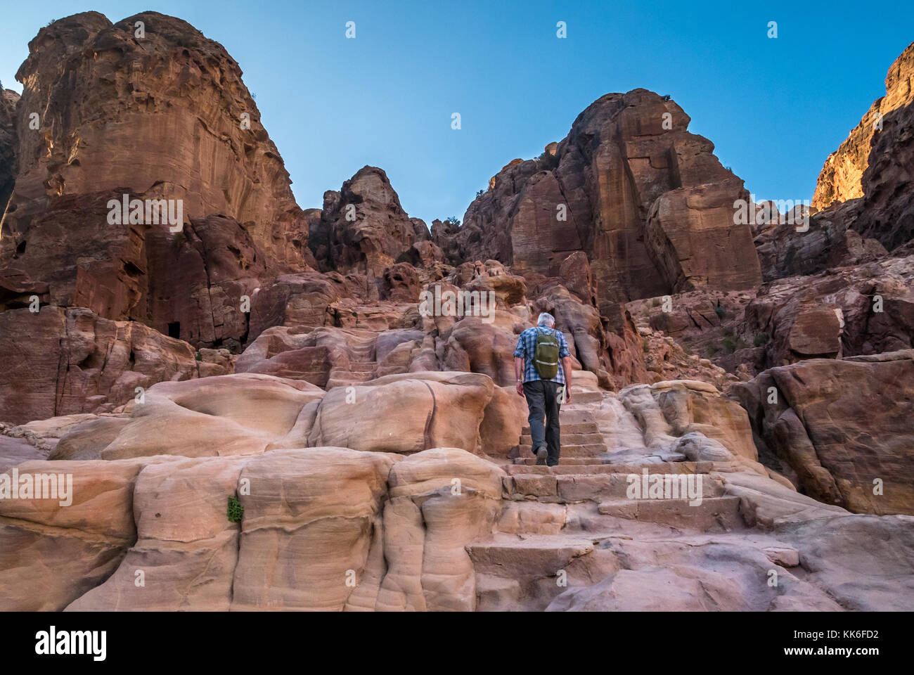 Senior man climbing carved stone steps on walking route to High Place of Sacrifice, Petra, Jordan, Middle East, in early morning light with blue sky Stock Photo