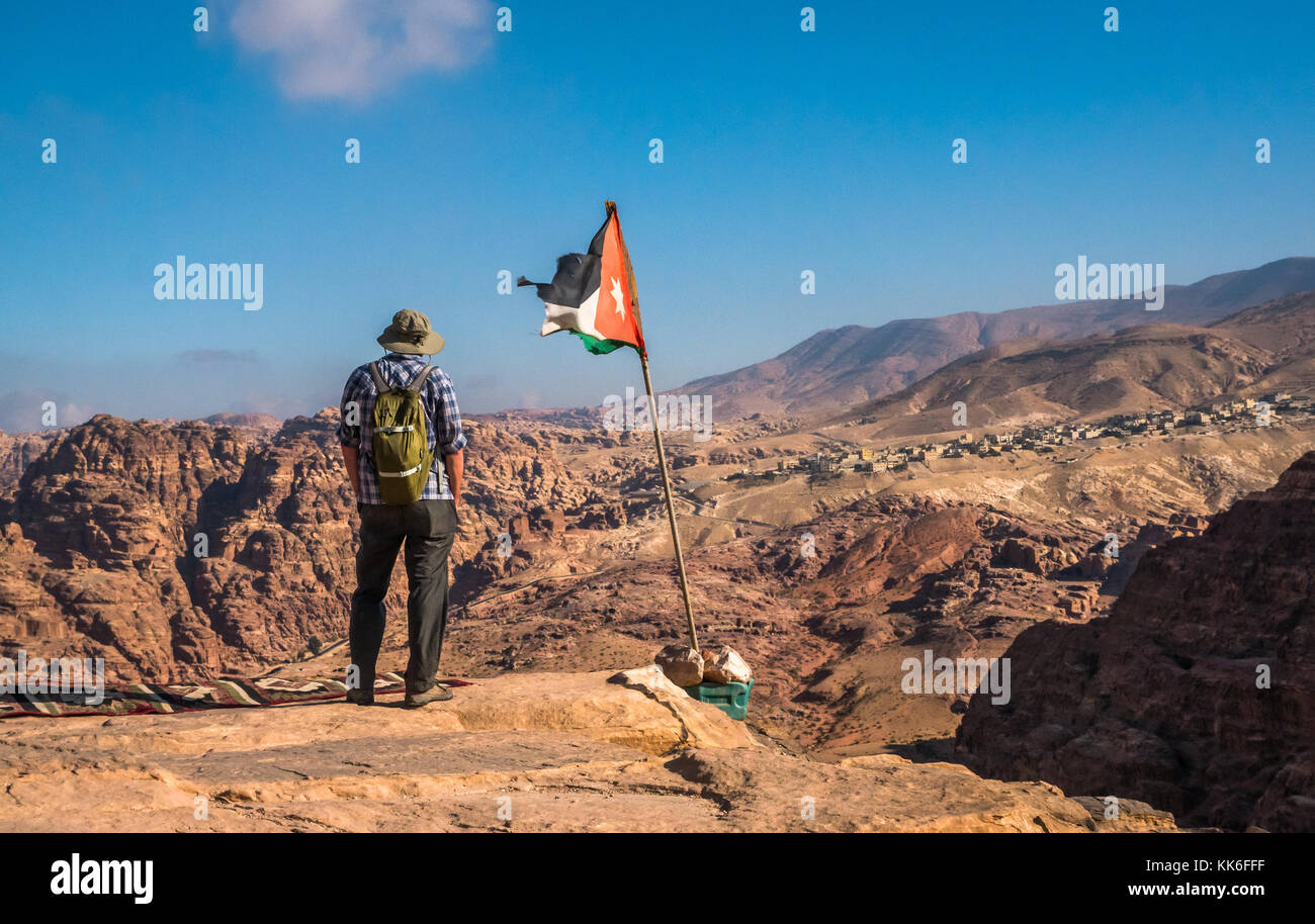 Senior man in 60s standing at cliff edge at High Place of Sacrifice, overlooking Petra archaeological site with Jordanian flag, Jordan, Middle East Stock Photo