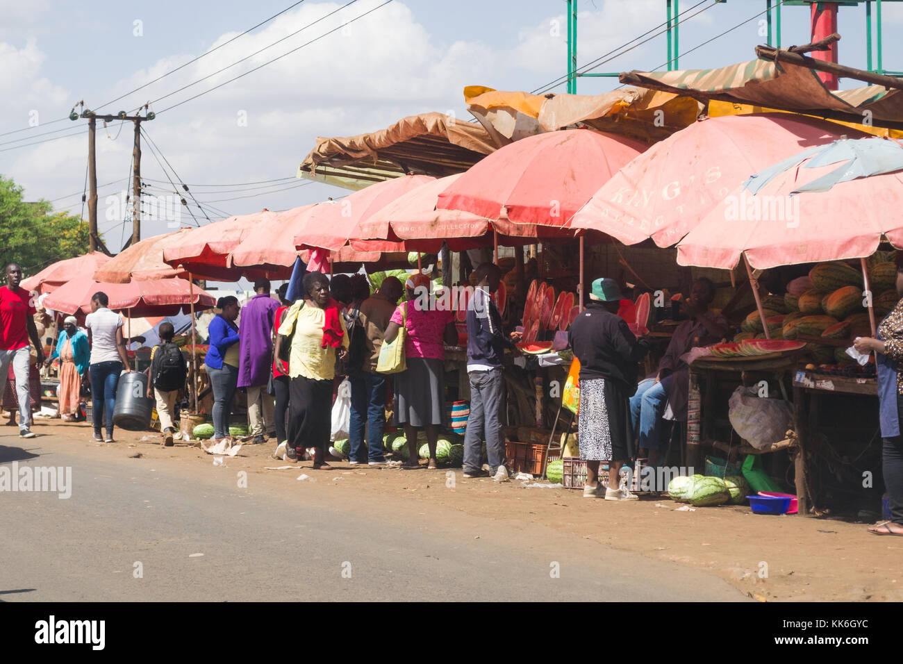 A busy roadside row of market stalls selling fruit and vegetables with people walking around, Kenya, East Africa Stock Photo