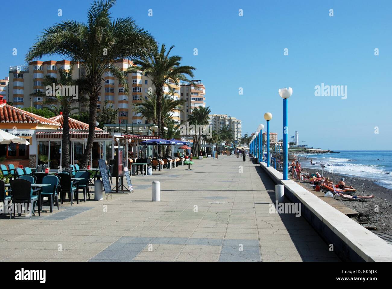 View along the promenade with pavement cafes to the left hand side and tourists relaxing the beach to the right, Torrox Costa, Malaga Province, Andalu Stock Photo