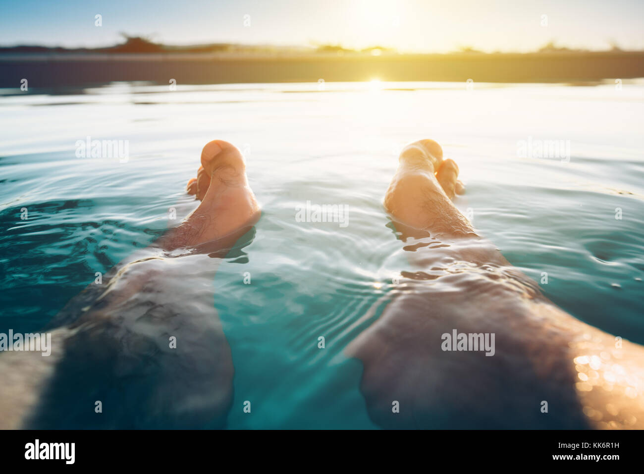Male feet in outdoor swimming pool. Man enjoying refreshing poolside water in summer sunset. Holidays vacations and weekend activities. Stock Photo