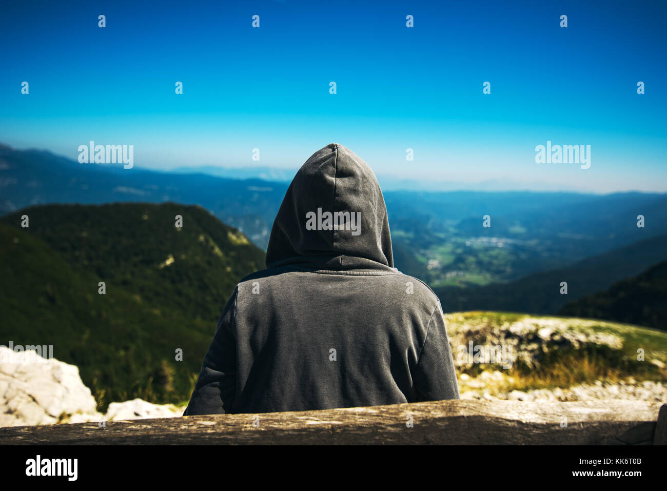 Mountain hiker at high viewpoint looking at the valley. Female tourist person in hooded jacket at mountain top enjoying the view. Stock Photo