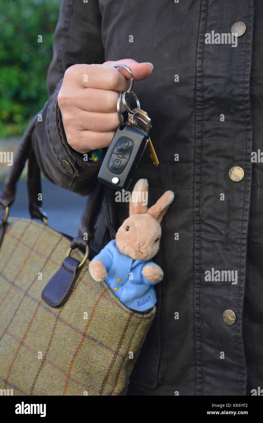 working mother, car keys in hand, with a child's toy rabbit sticking out of her bag Stock Photo