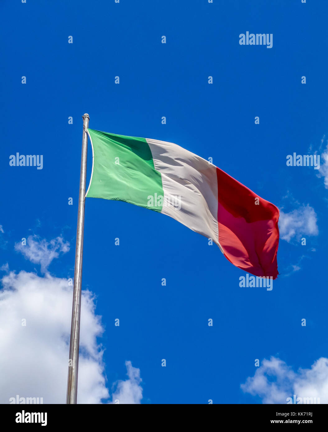An Italian Flag flying from a flag pole with a background of blue sky and cumulus clouds. Stock Photo