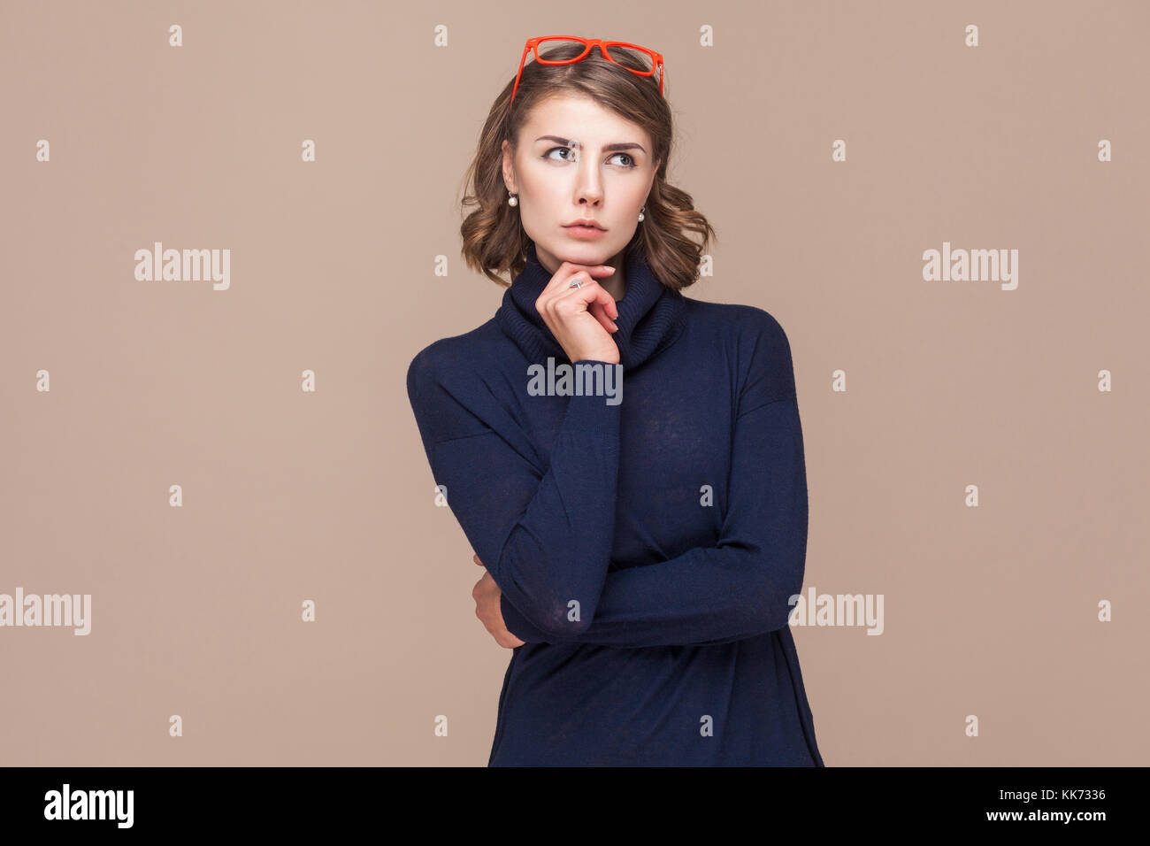 Thoughtful lady pondering and touching chin. Studio shot, light brown background Stock Photo