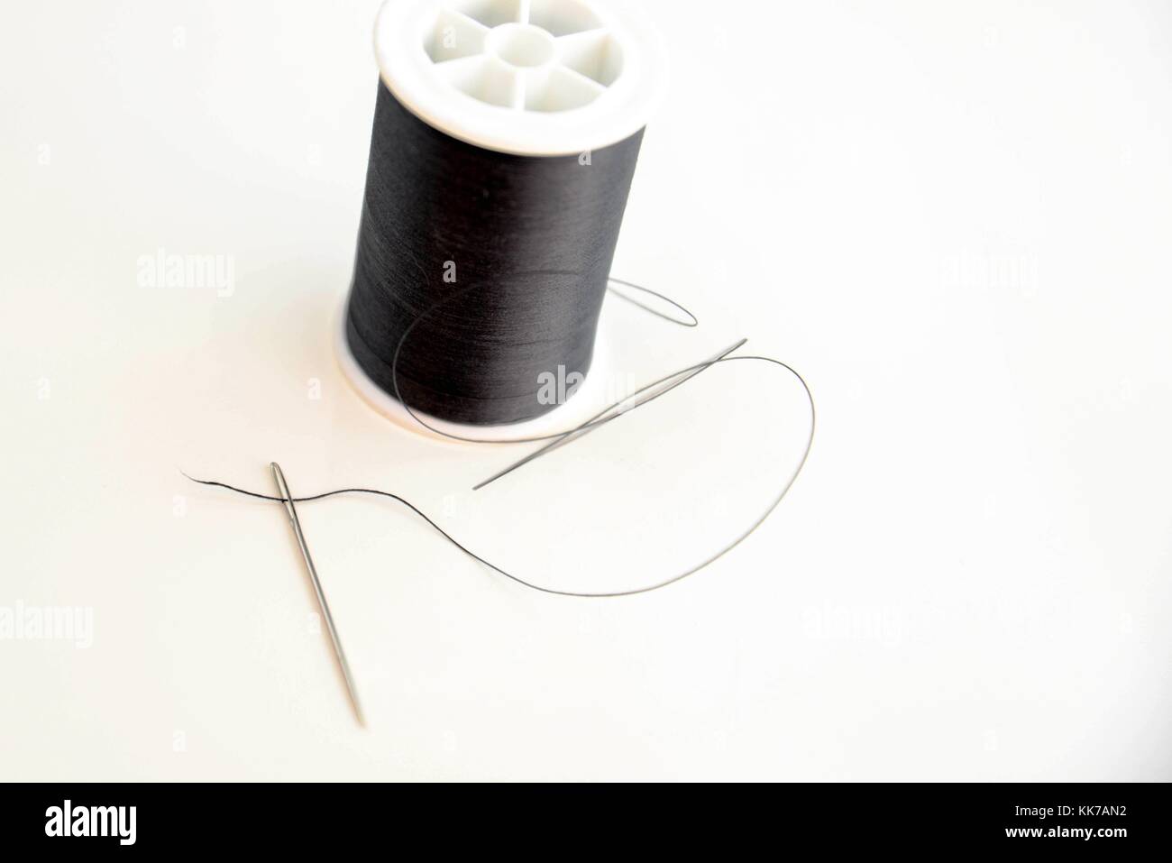 threaded needle and black spool of thread Stock Photo Alamy