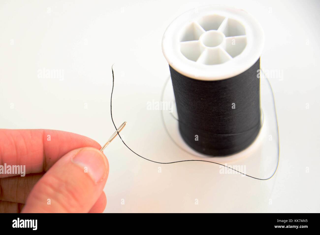 hand threading a needle with black thread Stock Photo - Alamy