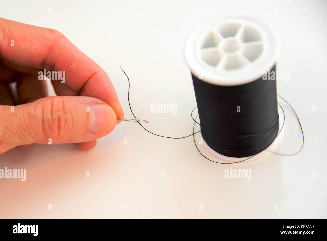 hand threading a needle with black thread Stock Photo Alamy