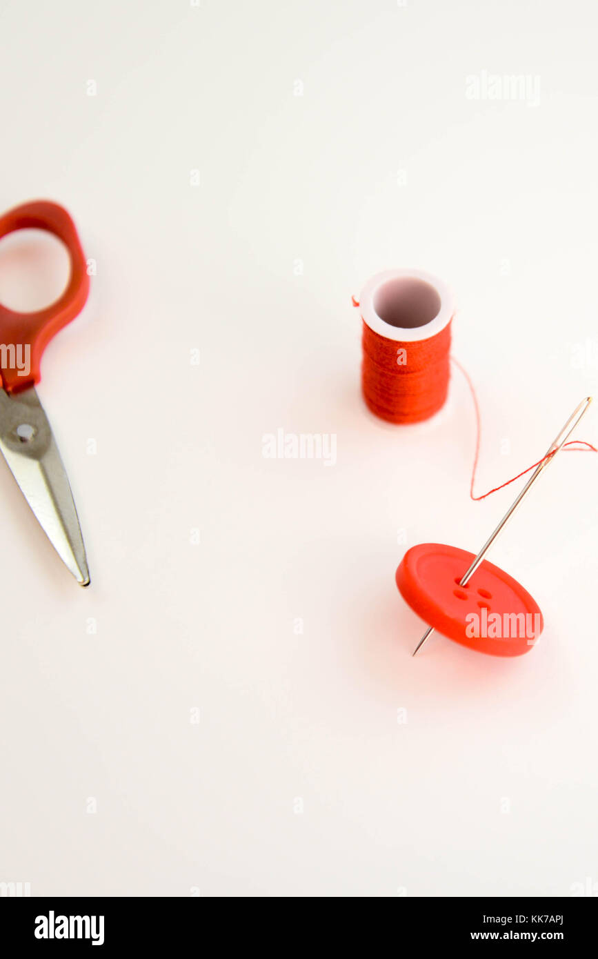 threaded needle, red spool of thread, red button, and red scissors ...