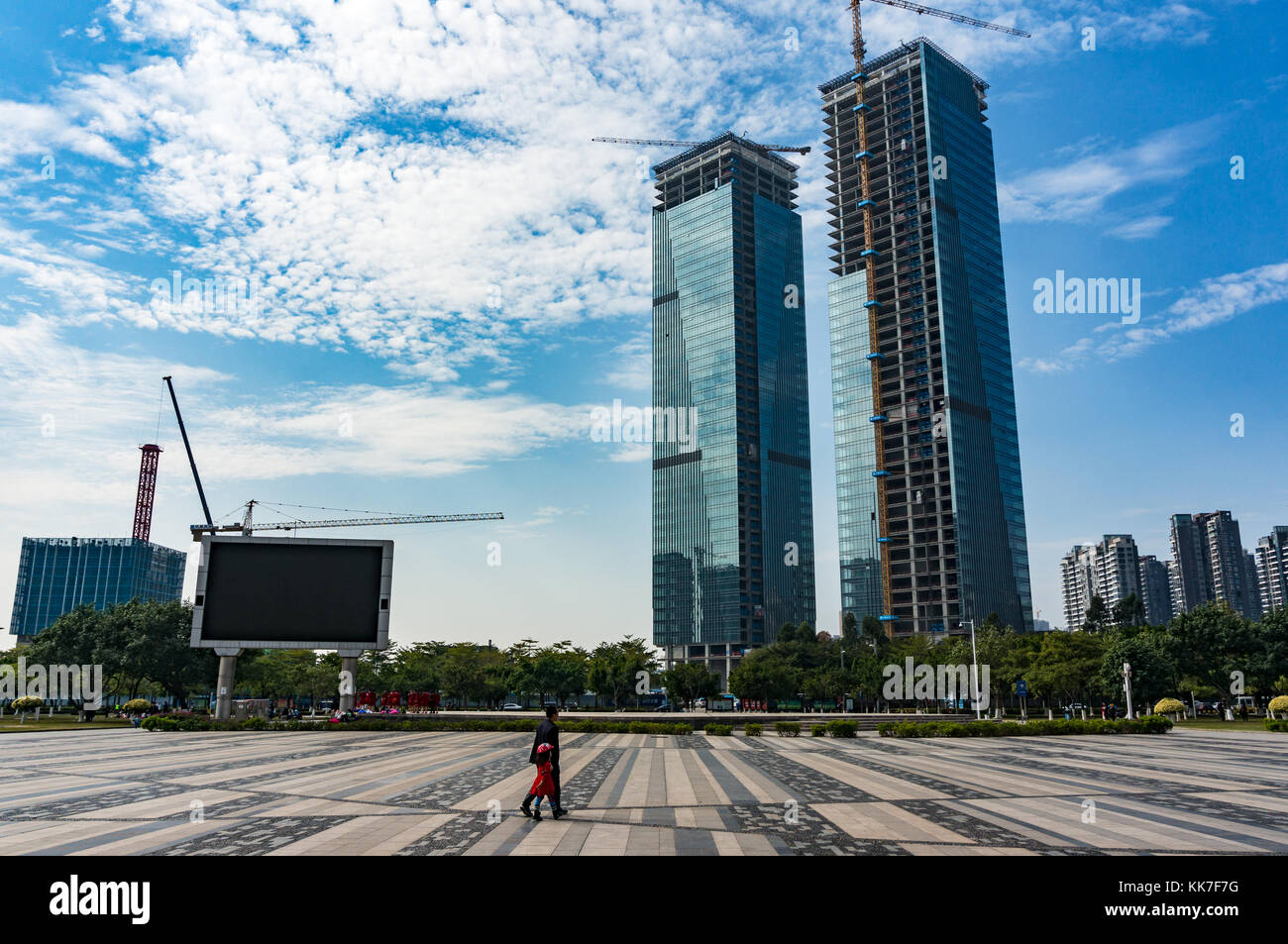 Father and daughter walking in vast city square as unfinished skyscrapers buildings loom in the distance in Shenzhen, Guangdong Province, China Stock Photo