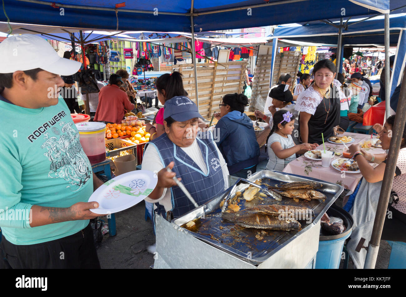 People buying and eating food including fish; Otavalo food market, Ecuador, South America. Stock Photo