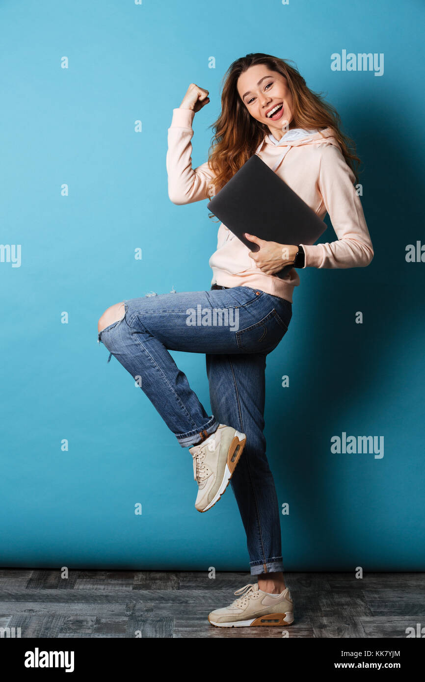 Full length portrait of a cheerful young girl holding laptop computer ...