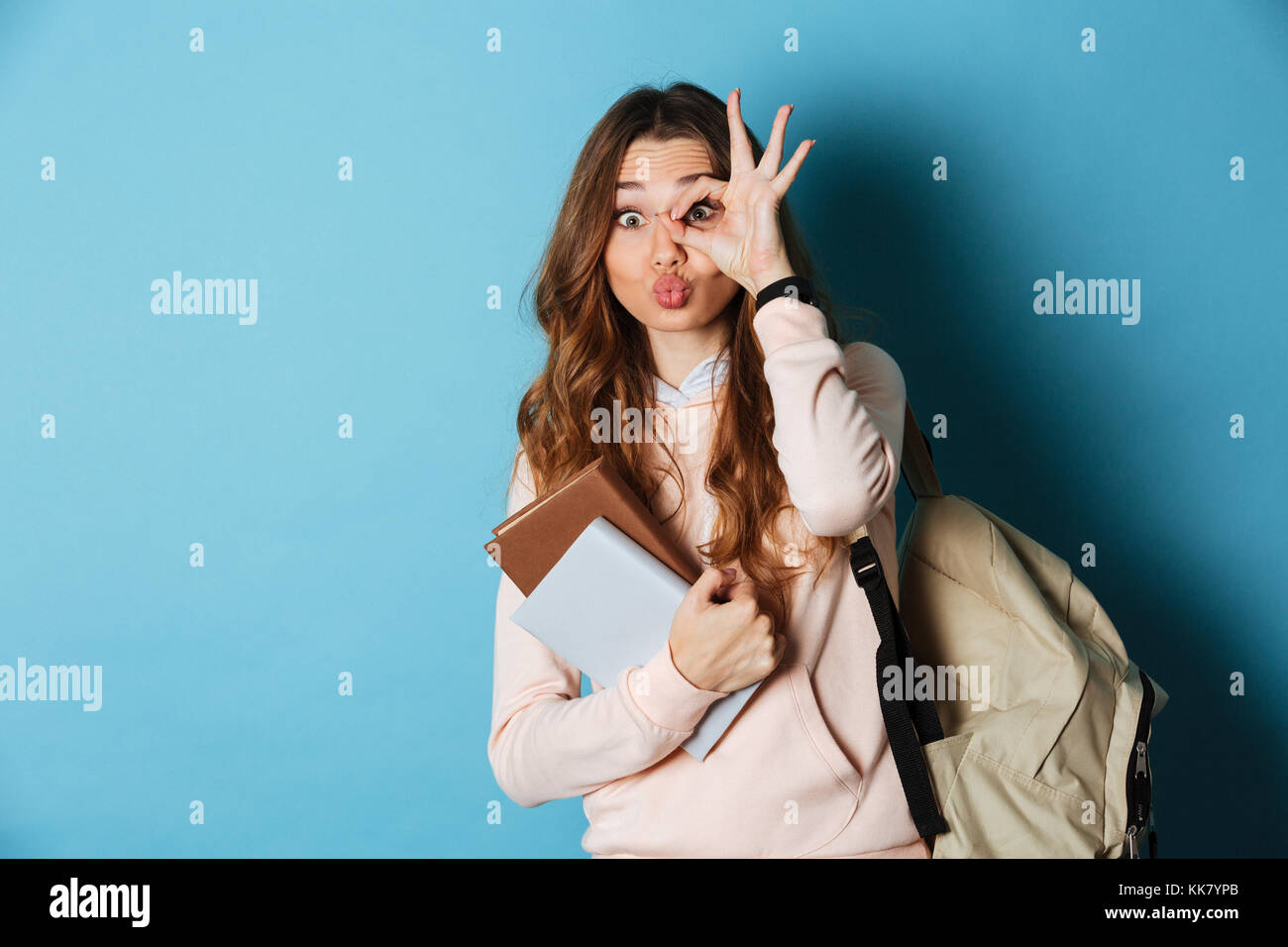 Portrait of a cheerful funny girl student with backpack holding books