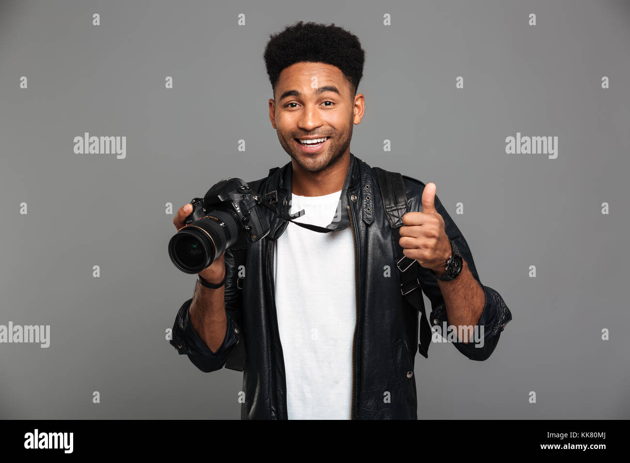 Young smiling afro american man holding photocamera and showing thumb up gesture, looking at camera, isolated on gray background Stock Photo