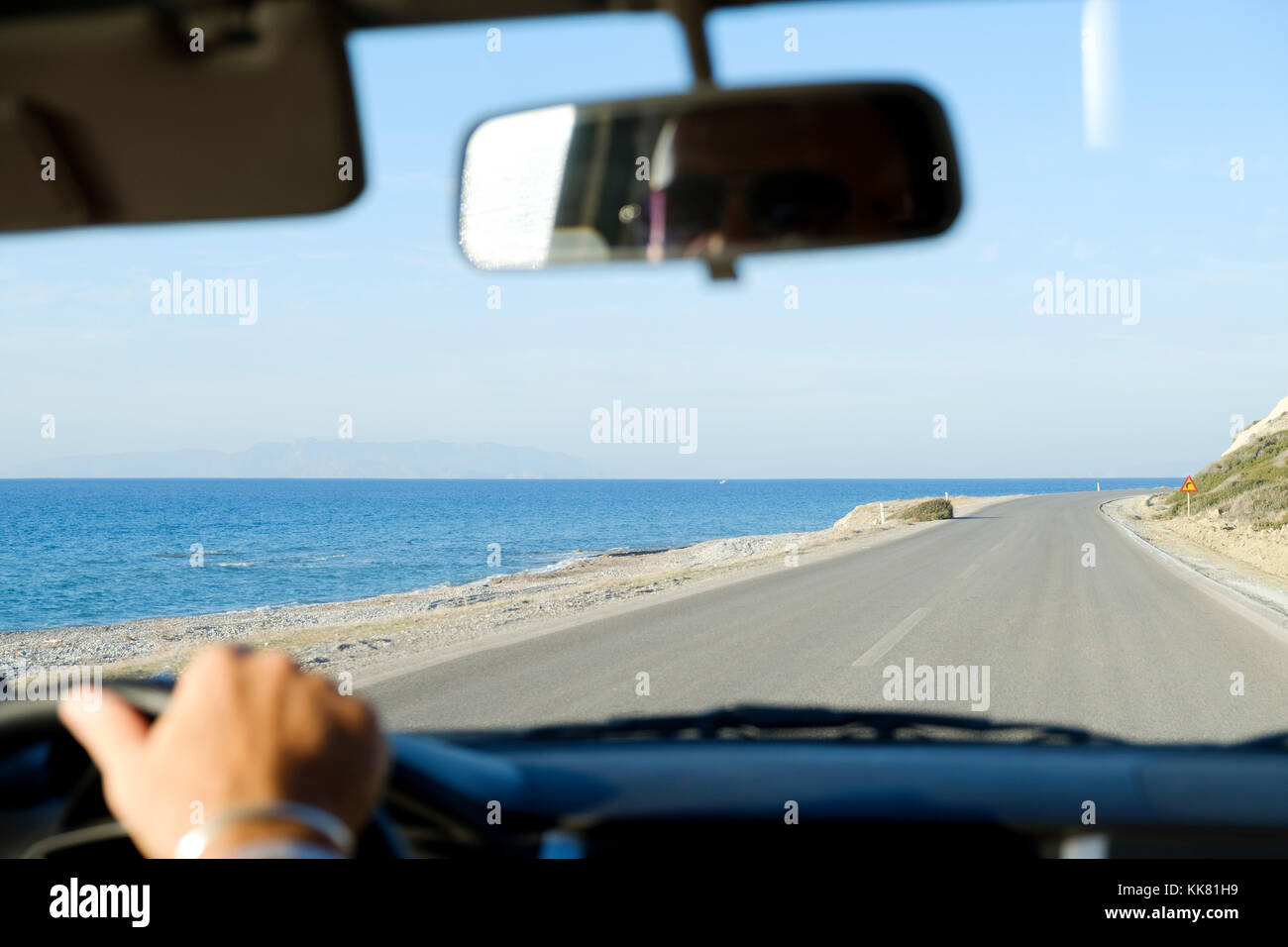 A view from within a car as its driven along a deserted coastal road with a sandy beach and the sea to the side of the road. Stock Photo