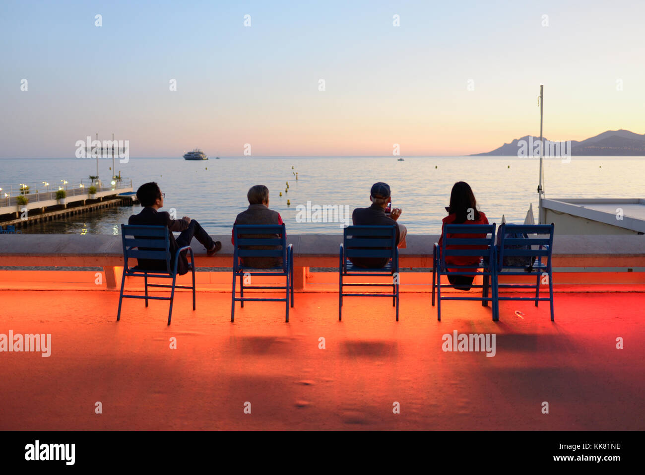 Four Tourists Enjoy the Sunset on the Boulevard de la Croisette, Cannes, at Dusk, with Dramatic Colour Street Lighting, French Riviera, france Stock Photo