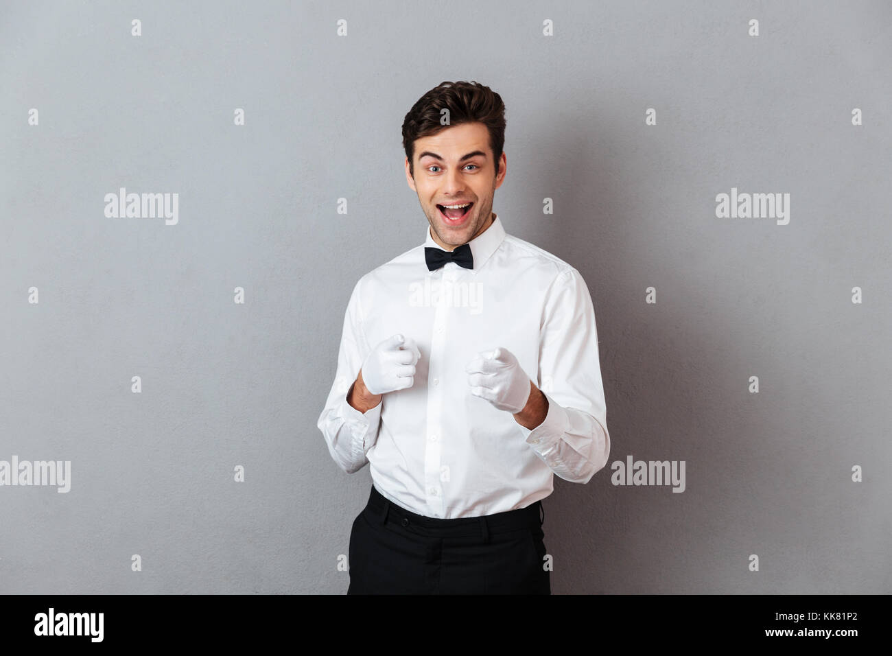Portrait of a cheerful young male waiter dressed in unifrom pointing two fingers up at camera isolated over gray background Stock Photo