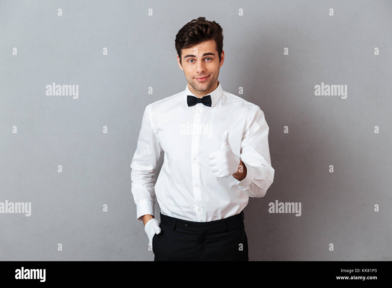 Portrait of a smiling young male waiter dressed in unifrom pointing finger at camera isolated over gray background Stock Photo