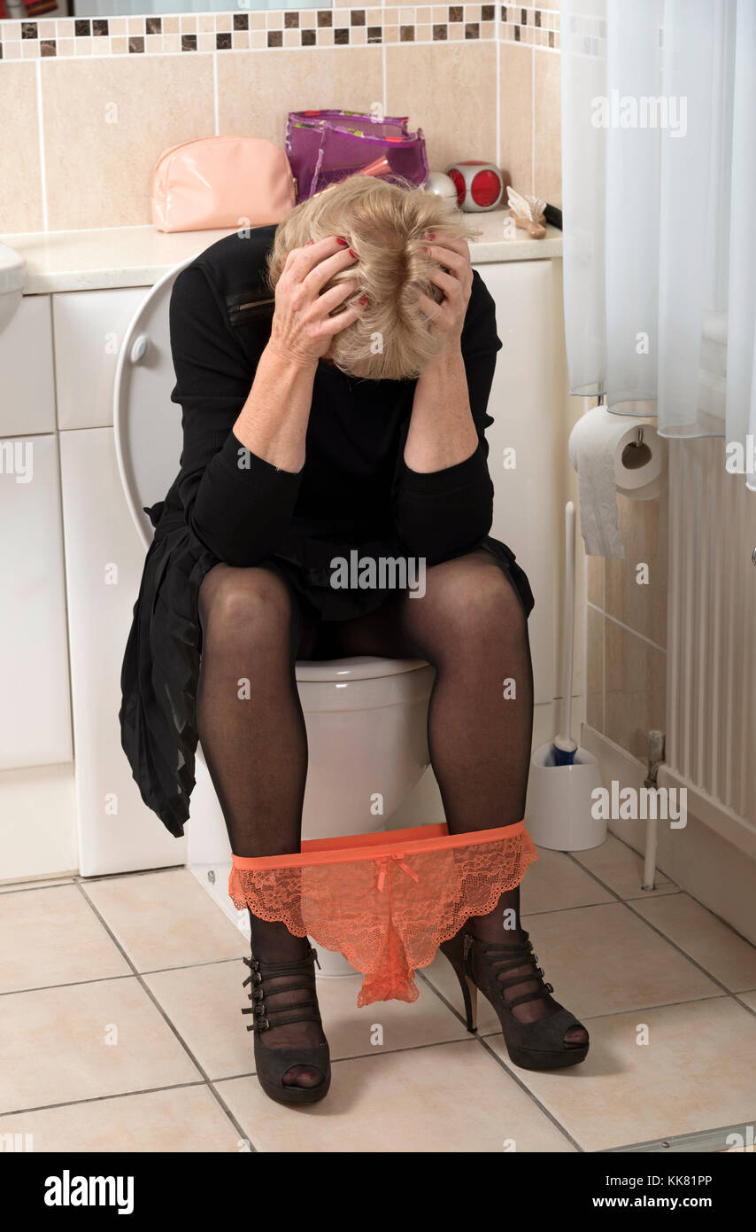 Distressed blond woman sitting on the toilet with hands on her head Stock Photo