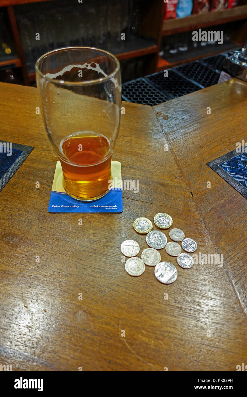 Nearly empty beer glass on bar counter with coins for another pint Stock Photo