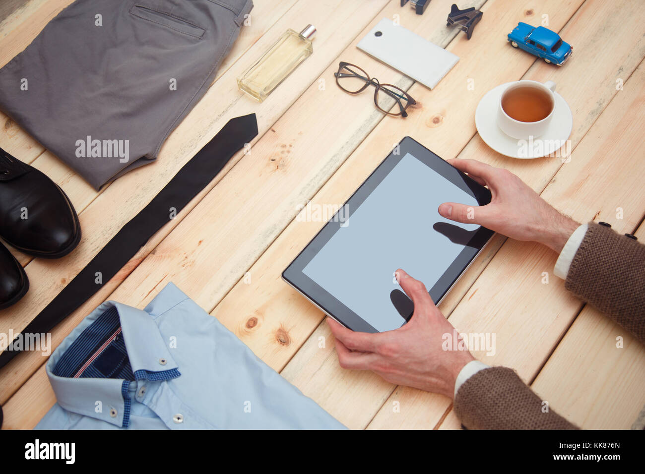 A businessman uses a tablet. The concept of men's online shopping. Fashionable clothes and accessories are on the table. Stock Photo