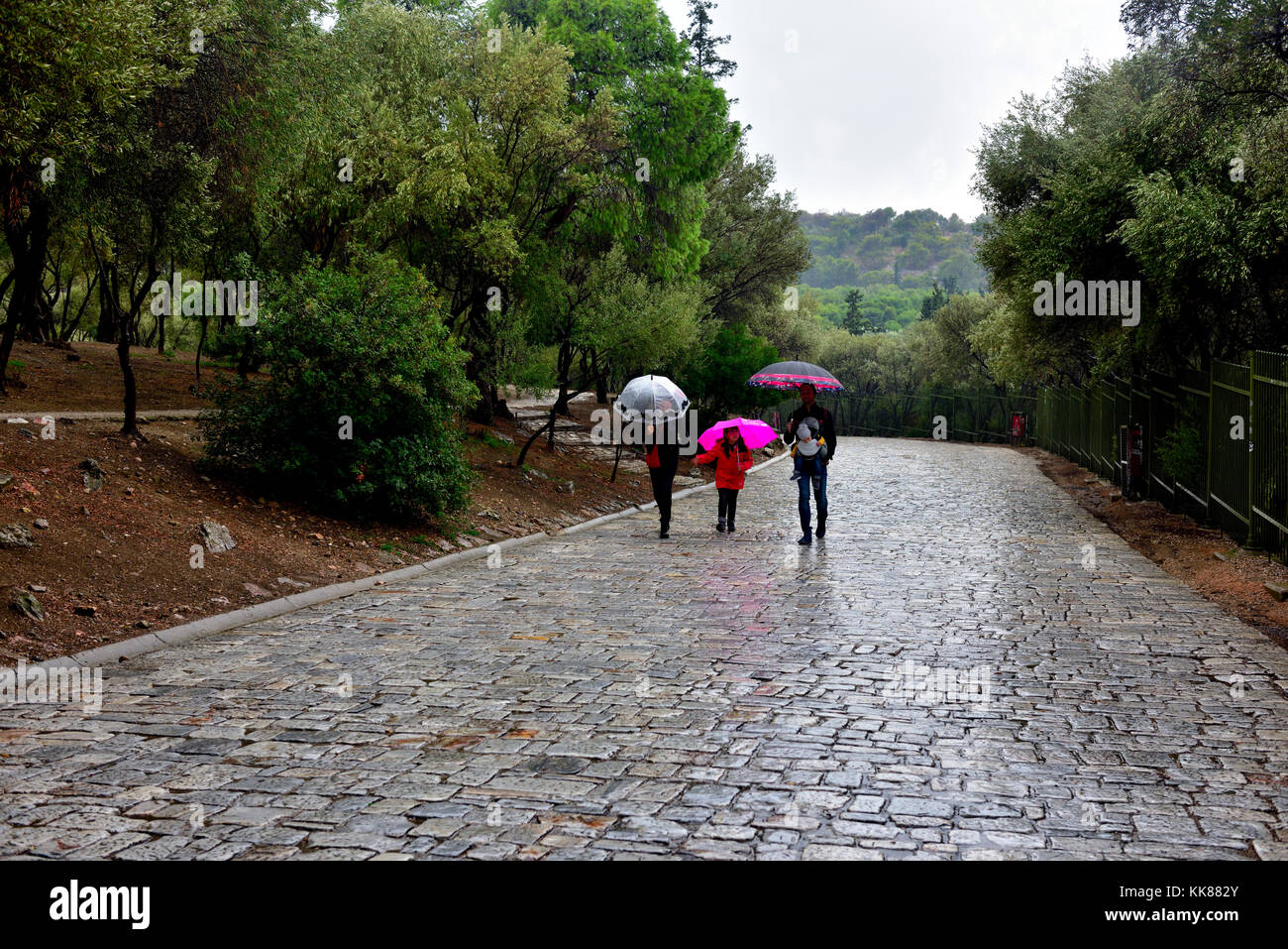 Three people with umbrellas on stone pathway in rain Stock Photo