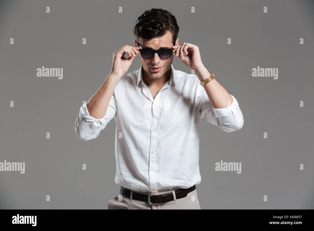 Portrait of a charming young man dressed in white shirt wearing eyewear ...