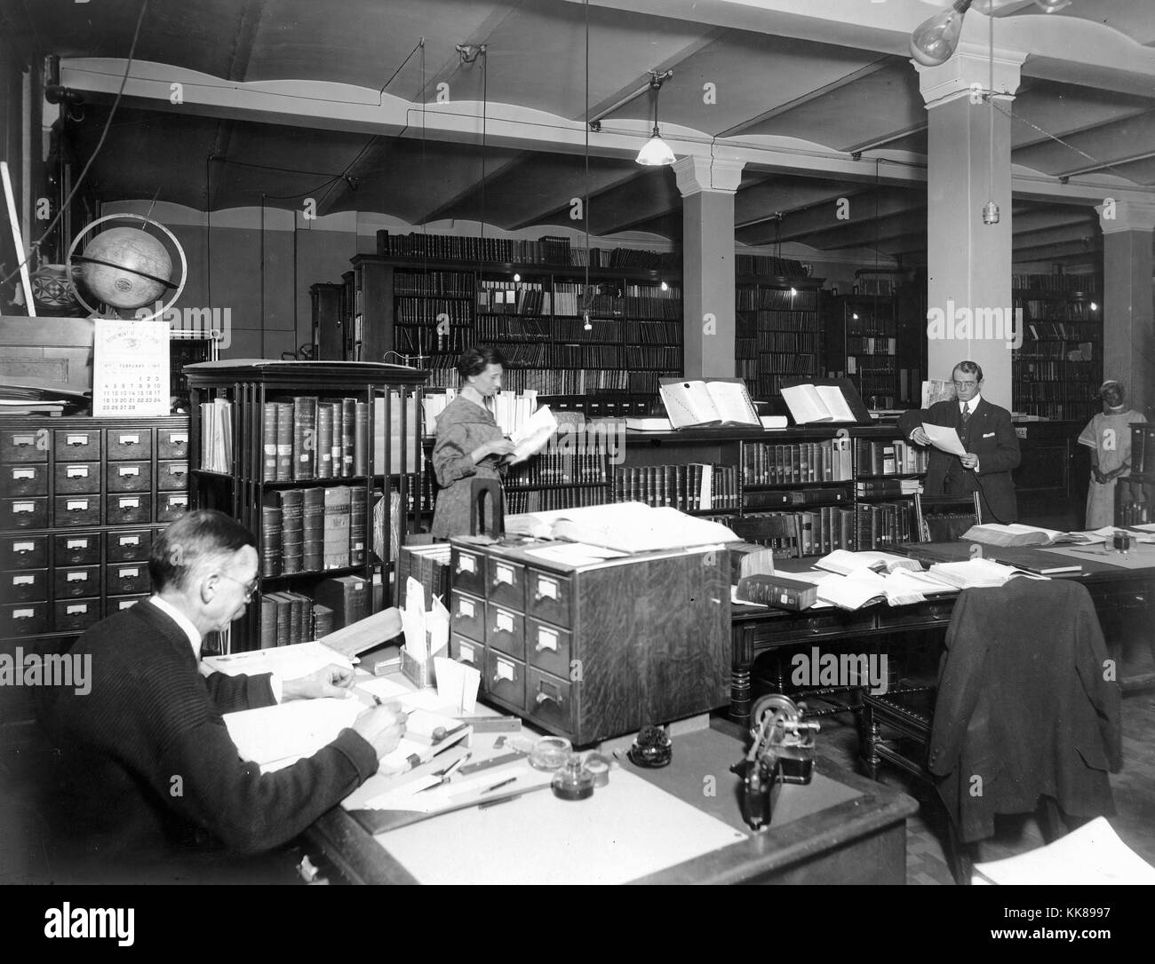 US Geological Survey library in Hooe Building, Washington DC. Note rotating bookcase at left, next to card catalogs, left to right: J.M. Nickles, J.L.V. McCord original Survey librarian, J.E. Latimer, and Mary Coats. Image courtesy USGS. 1917. Stock Photo