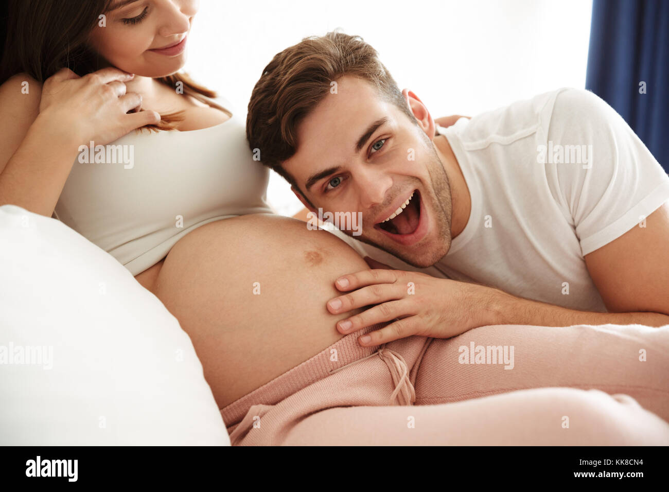 Happy young man listening his pregnant wifes belly while lying ...