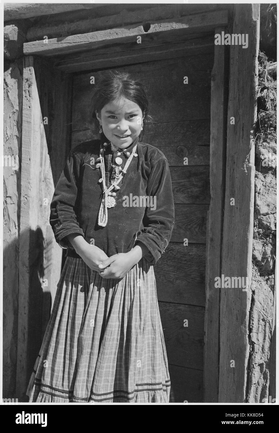 Black and white photograph of a young Native American girl standingg in front of a doorway, captioned 'Navajo Girl, Canyon de Chelle, Arizona', by Ansel Adams, from Photographs of National Parks and Monuments, Canyon de Chelly National Monument, Arizona, United States, 1941. Stock Photo