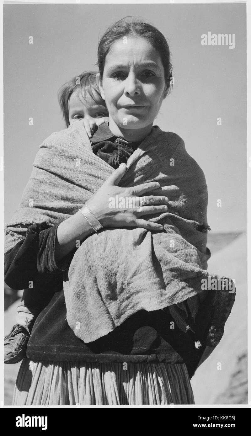 Black and white photograph of a Native American woman, toddler on her back, captioned 'Navajo Woman and Child, Canyon de Chelle, Arizona', by Ansel Adams, from Photographs of National Parks and Monuments, Canyon de Chelly National Monument, Arizona, United States, 1941. Stock Photo