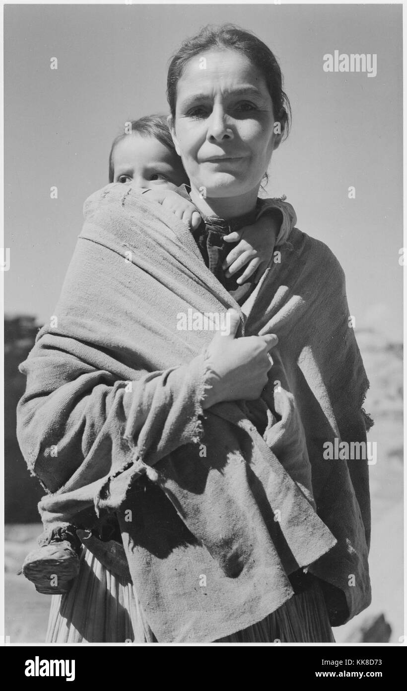 Black and white photograph of a Native American woman, toddler on her back, captioned 'Navajo Woman and Child, Canyon de Chelle, Arizona', by Ansel Adams, from Photographs of National Parks and Monuments, Canyon de Chelly National Monument, Arizona, United States, 1941. Stock Photo