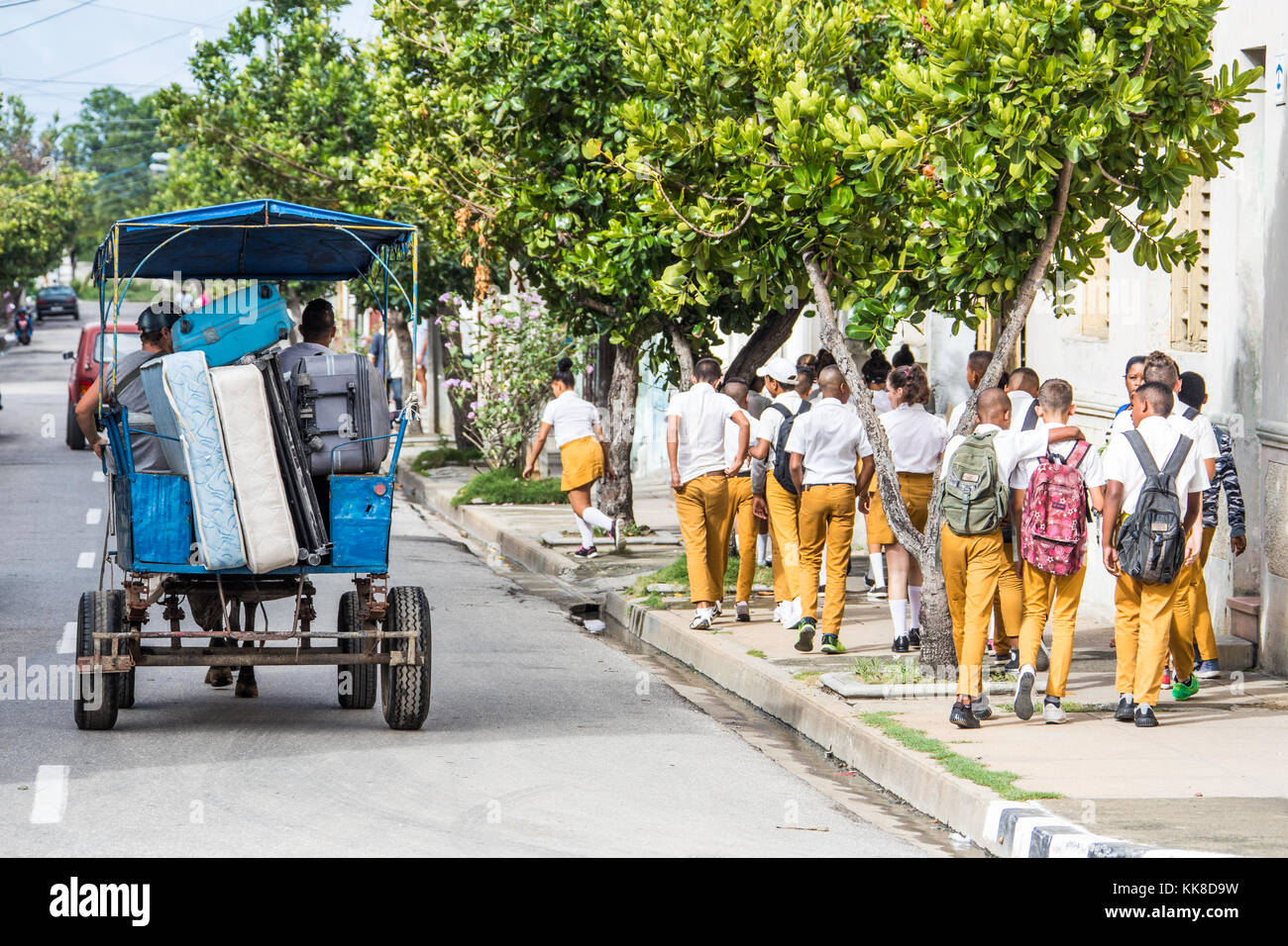 Students walking to school berside a horse carriage moving possessions, Cienfuegos, Cuba Stock Photo