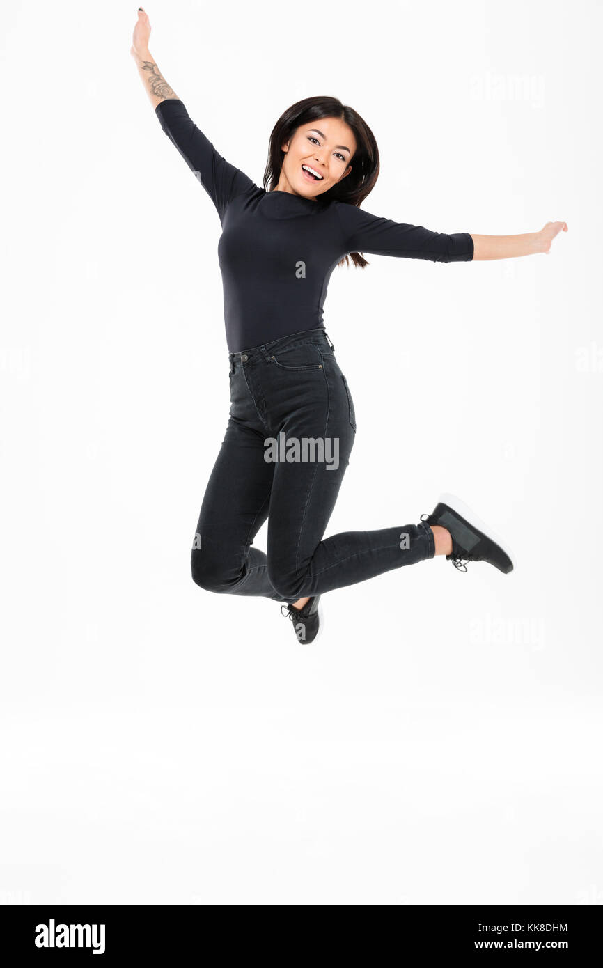 Picture of smiling young asian woman jumping isolated over white background. Looking camera. Stock Photo