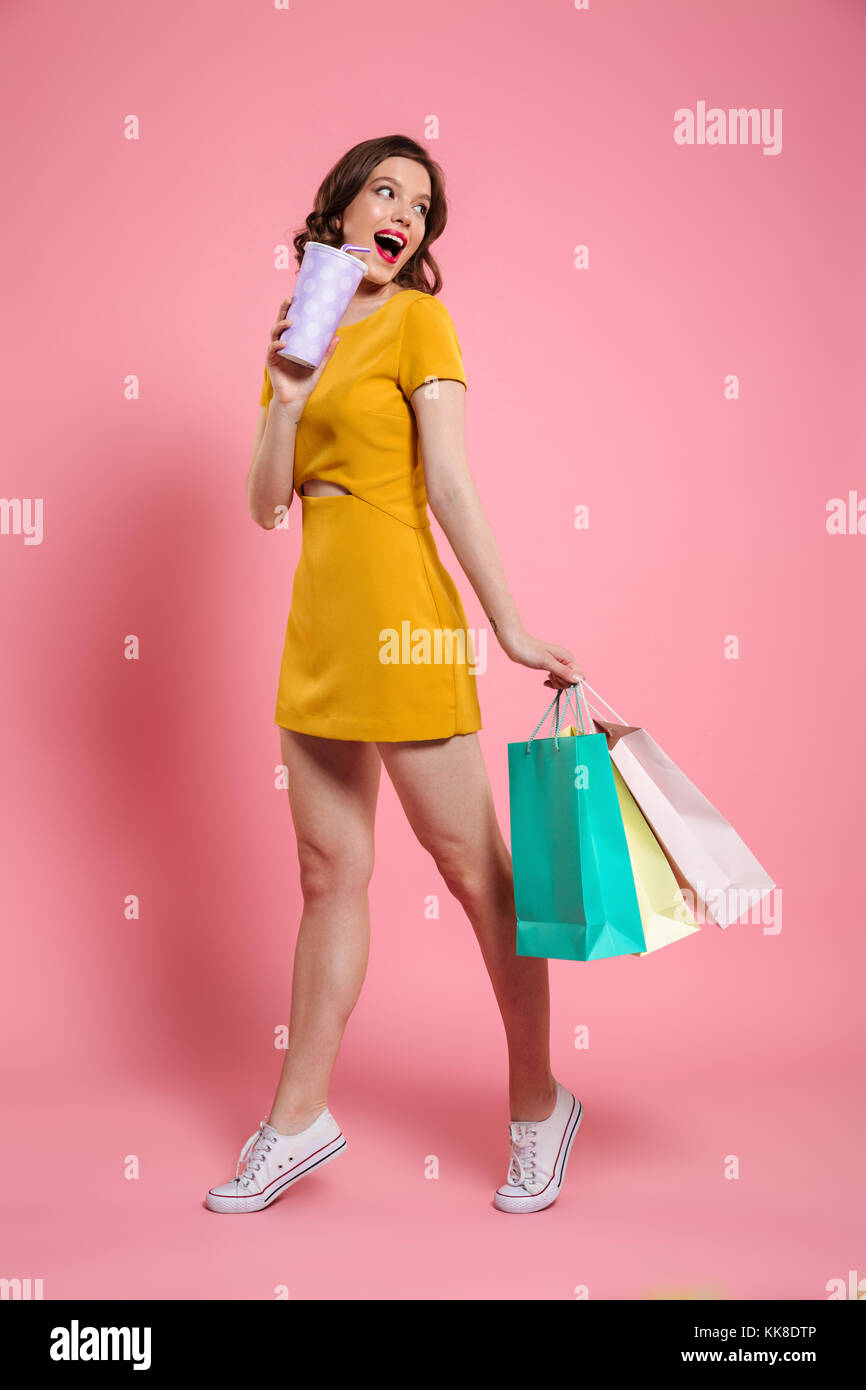 Full length portrait of a smiling young woman in dress holding shopping ...