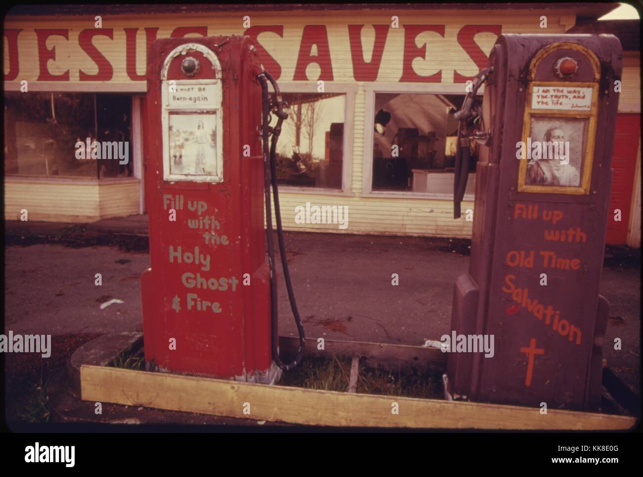 Color photograph of an abandoned gas station being used as a billboard for religious messages, the Station reads 'Jesus Saves', and the pumps read 'Fill up with Old Time Salvation' and 'Fill up with the Holy Ghost Fire', April, 1974. Image courtesy National Archives. Stock Photo