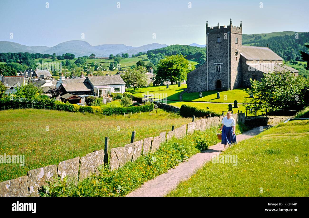 English village of Hawkshead in the Lake District National Park, Cumbria. Woman walking along path by St Michael's parish church Stock Photo