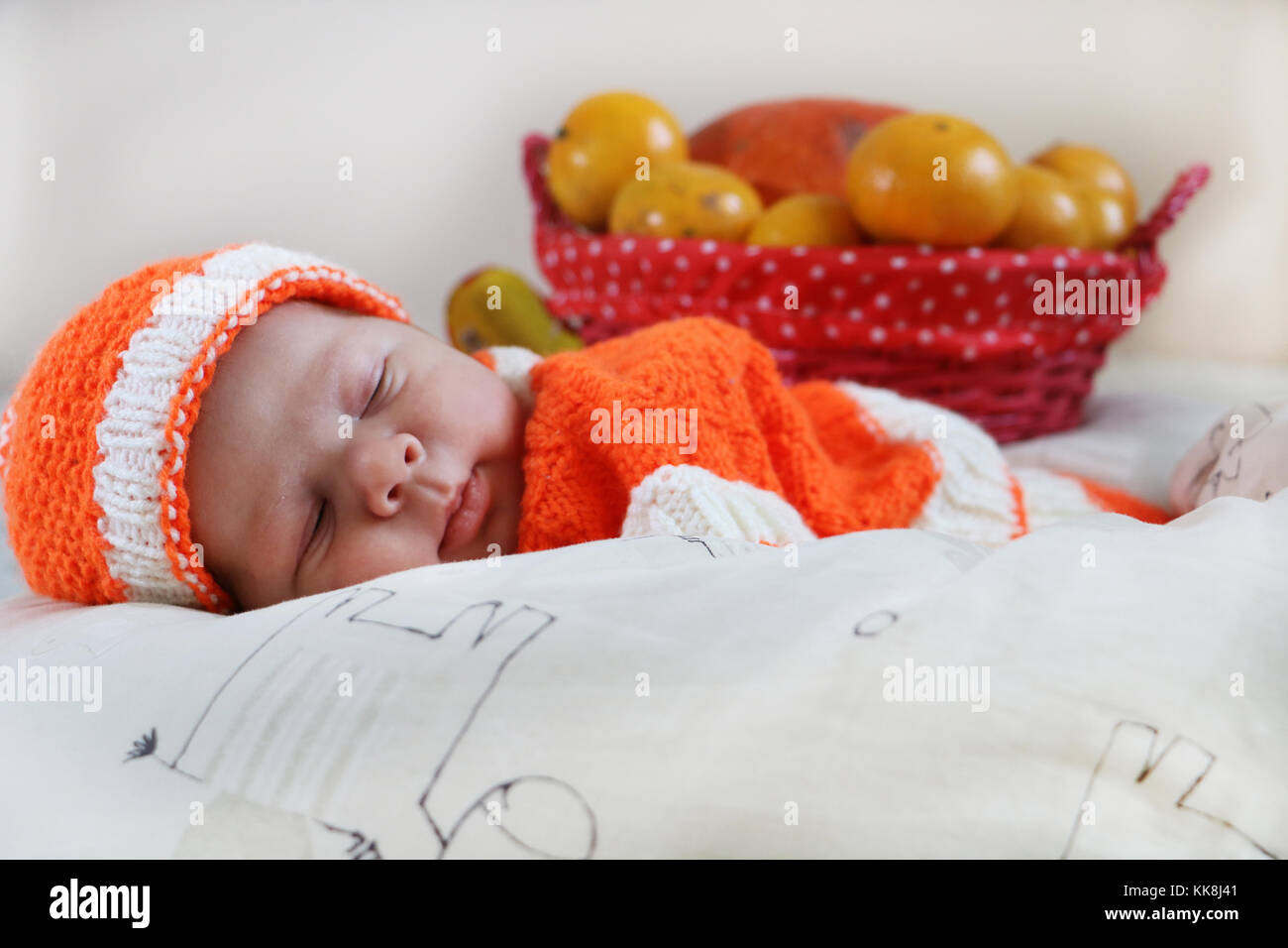 Cute sleeping newborn baby dressed in a knitted orange costume with pumpkin and oranges in