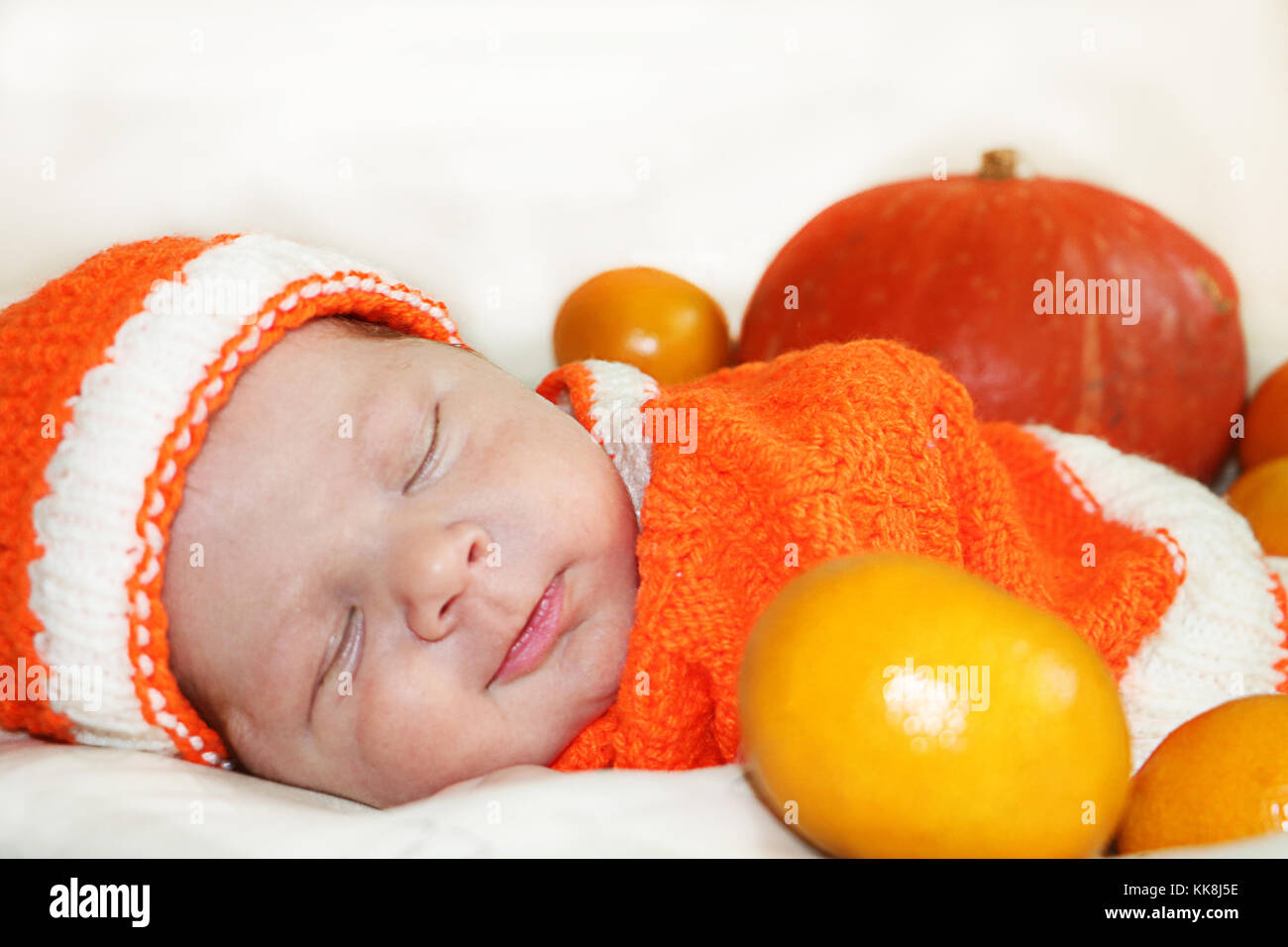Cute sleeping smiling  newborn baby dressed  in a knitted orange costume with pumpkin and oranges background. Autumn halloween or harvest concept. Smi Stock Photo