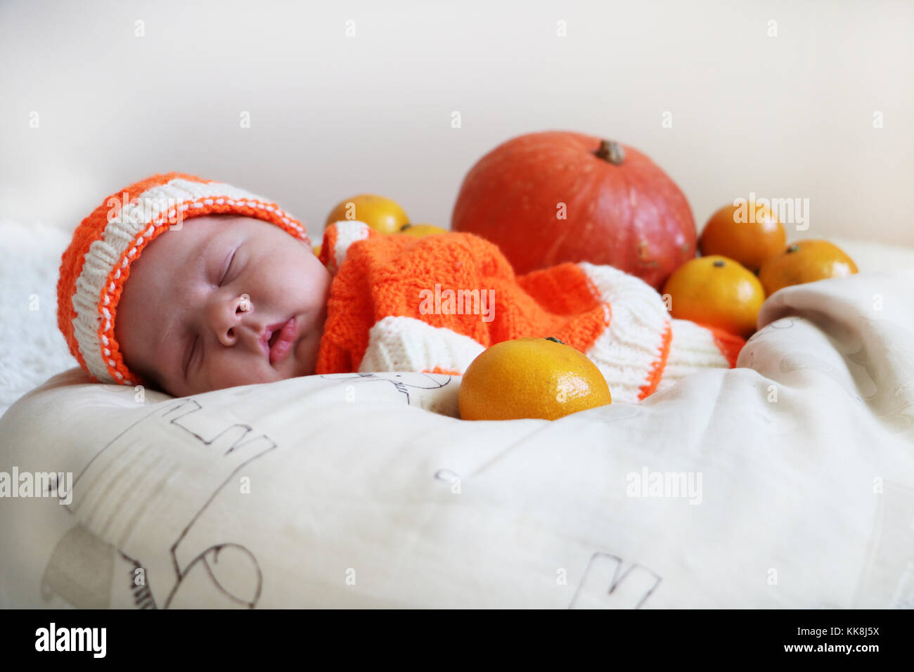 Cute sleeping newborn baby  in a knitted pumpkin or orange costume on pumpkin and oranges background. Autumn halloween or harvest concept. Stock Photo