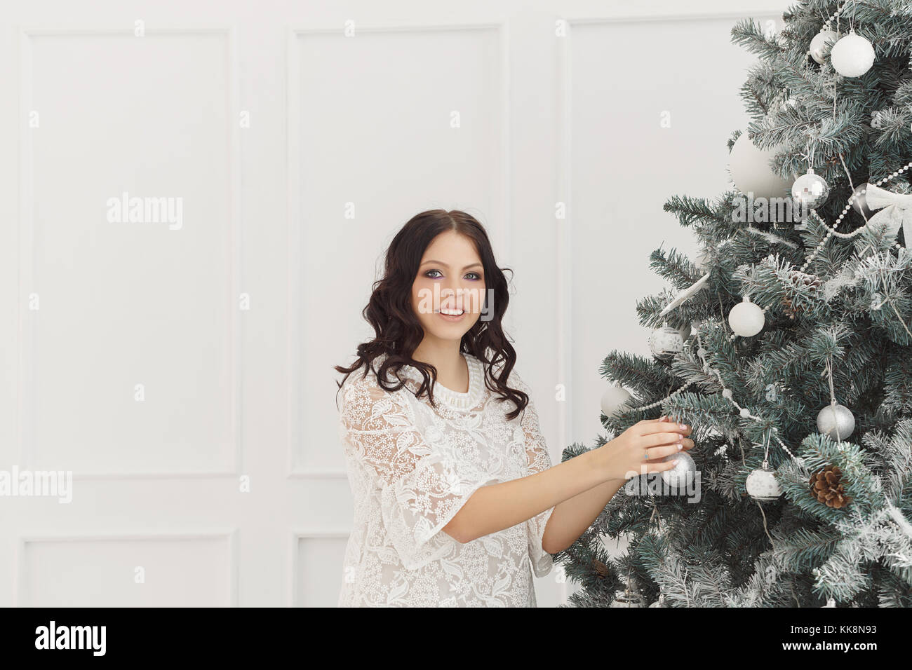 A cute teen girl holding a Christmas tree decorating balls. She is wearing a white dress. Stock Photo