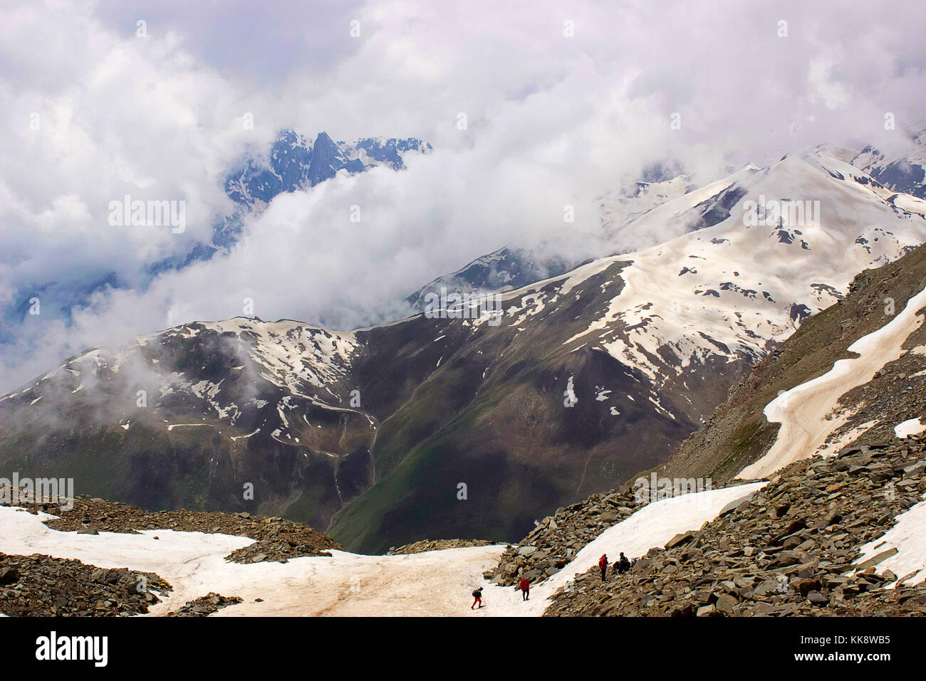 Clouds and snow clad mountains becoming one and trekkers at the base. Himachal Pradesh, Northern India Stock Photo