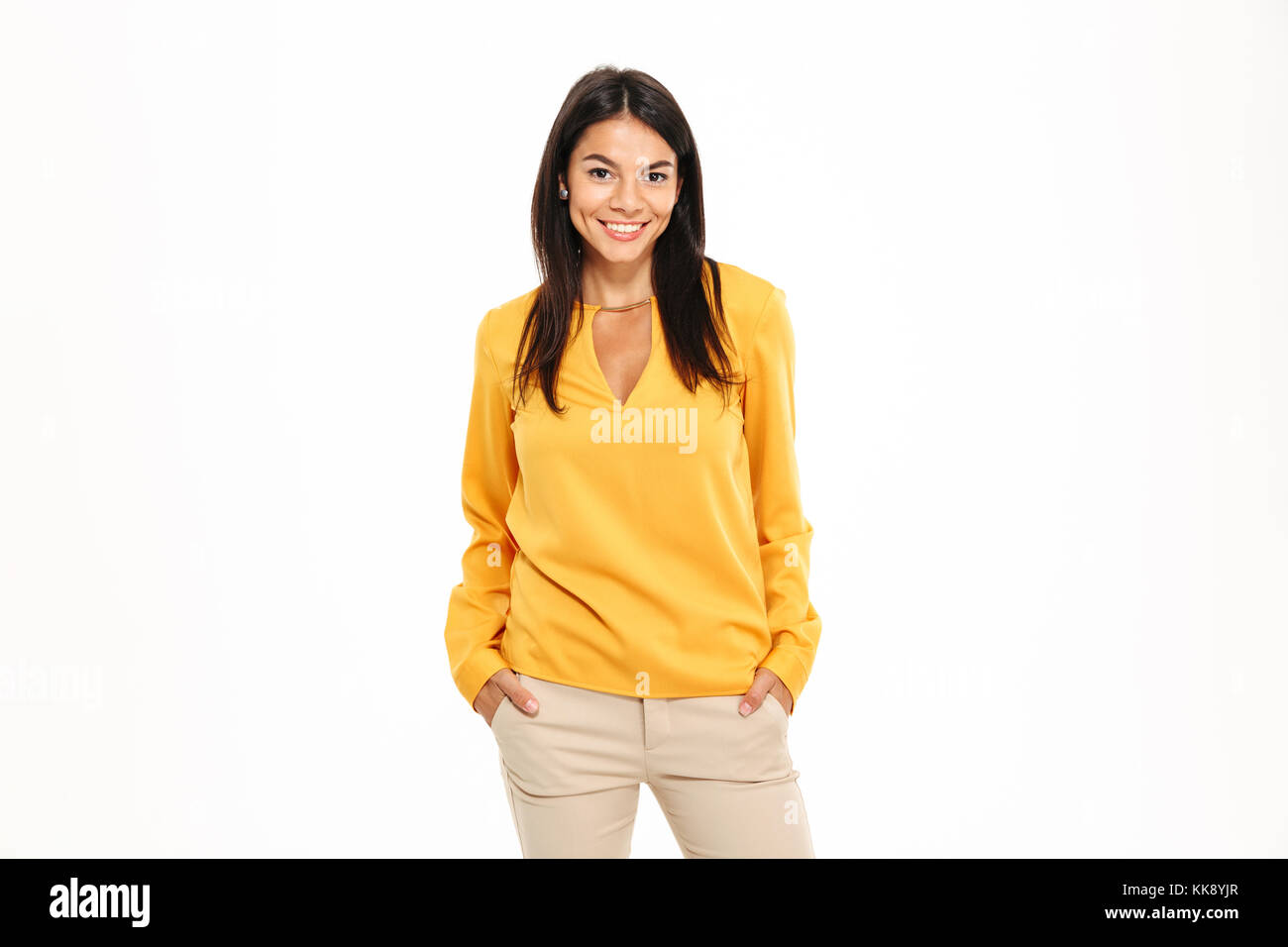 Portrait of a smiling young woman standing with arms in pockets and ...