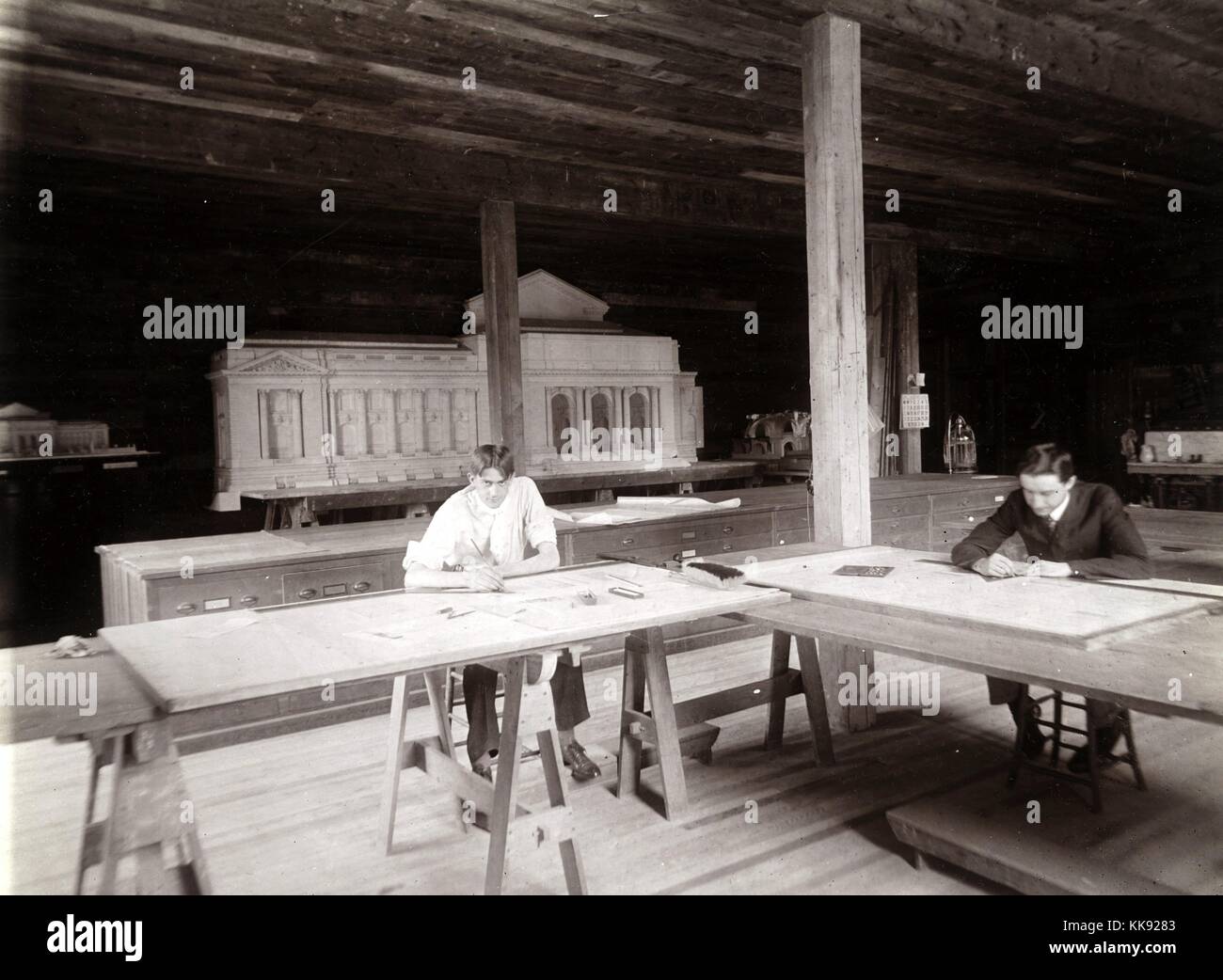 A photograph of two young architects working for Carrere and Hastings in their workshop, the founders of the firm both studied in France and became leaders in the Beaux-Arts architecture style, they previously wokred for the firm McKim, Mead and White before forming their own firm, a model of the main branch of the New York Public Library stands in the background, New York, New York, United States, 1905. From the New York Public Library. Stock Photo