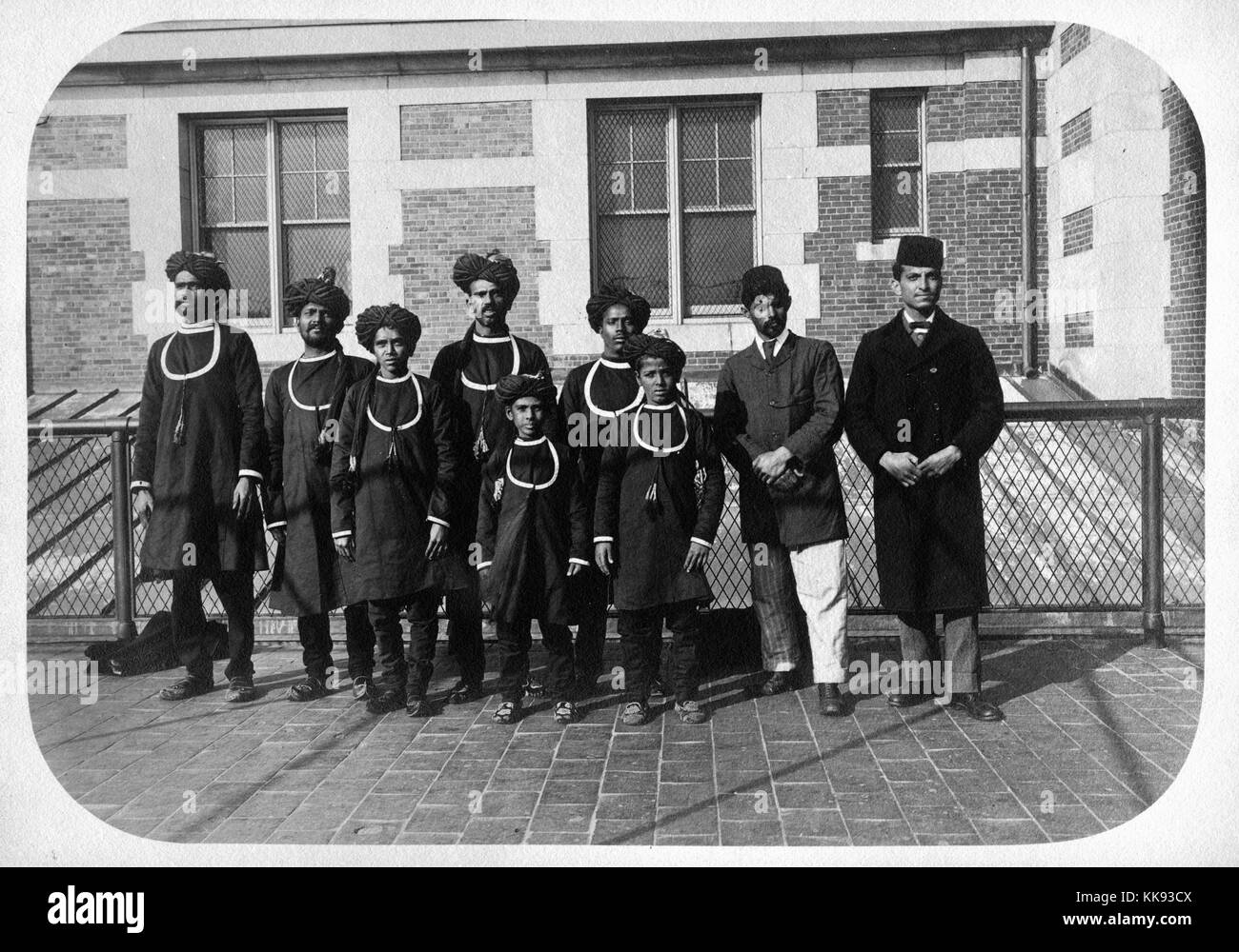 A photograph of a group of immigrants that have arrived on Ellis Island, the majority of the group are wearing long, robe-like tops and turbans, the two men on the right wear jackets and fezzes, New York, 1907. From the New York Public Library. Stock Photo