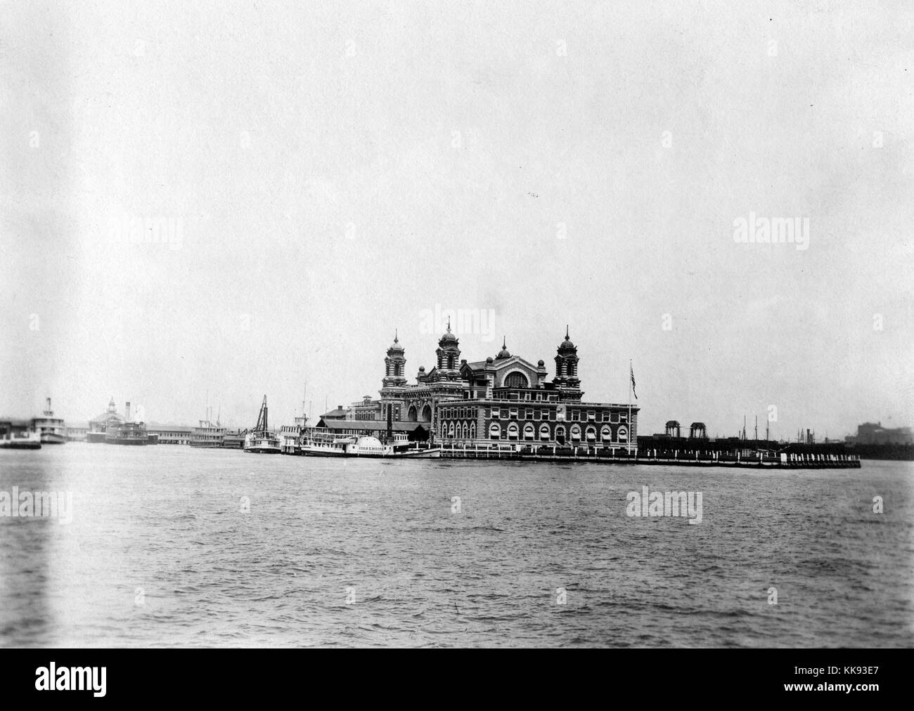 A photograph taken from the Upper New York Bay of the exterior of the Ellis Island immigration inspection station, the French Renaissance Revival building is constructed with red bricks and limestone trim, the building was first opened on December 17, 1900, it was closed in 1954 after processing over 12 million immigrants entering the United States, towers can be seen at the corners of the central portion of the structure, New York, 1907. From the New York Public Library. Stock Photo